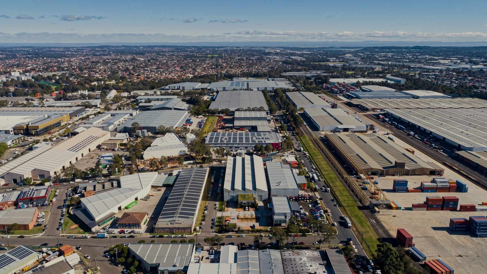 Aerial view over the Yennora industrial precinct in western Sydney, warehouse roofs and container yards to the horizon